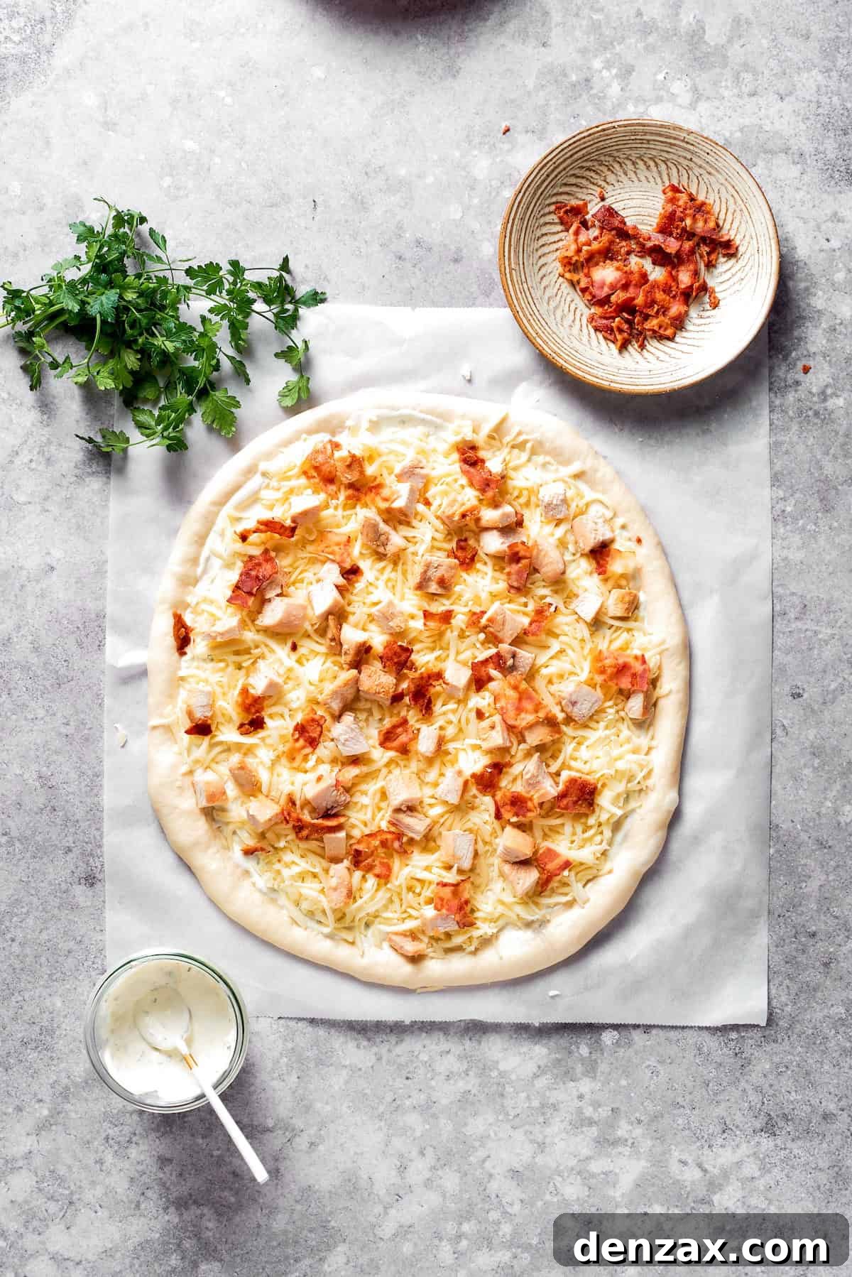 Bacon is added to the top of a chicken bacon ranch pizza.