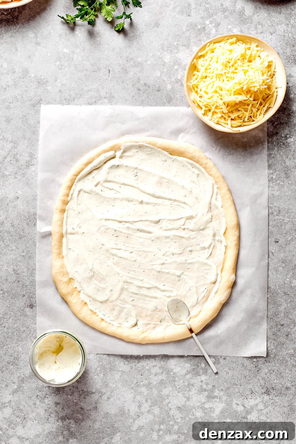 A circle of pizza dough is topped with ranch dressing.