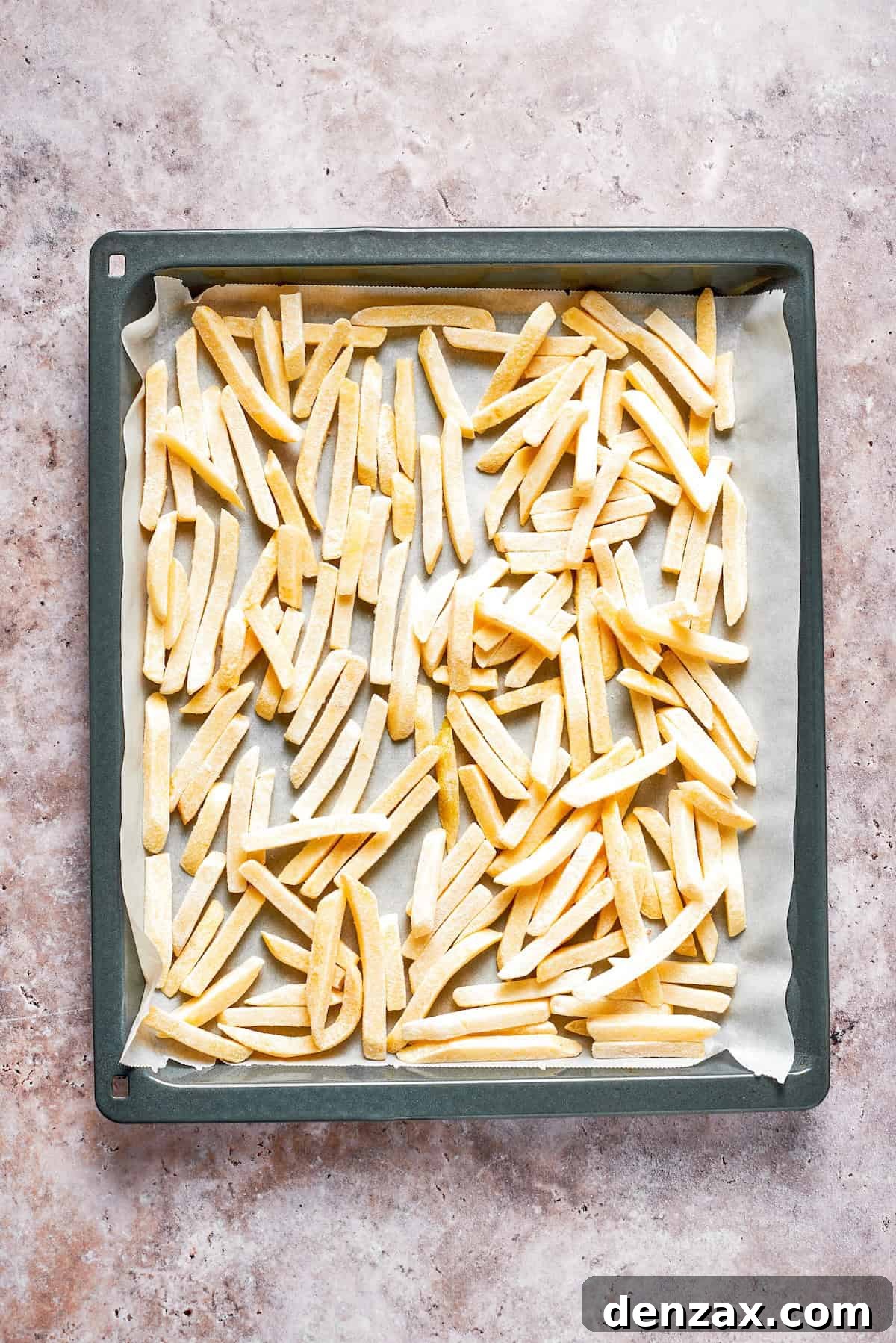 Frozen french fries spread out on a lined baking sheet.