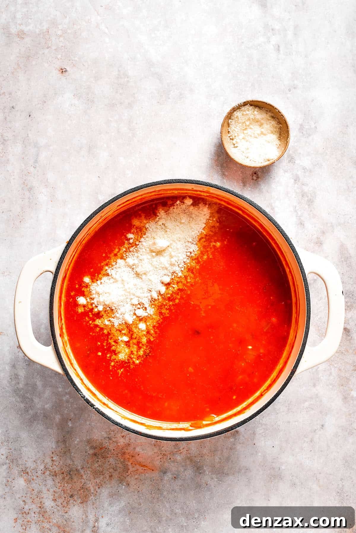 Parmesan cheese is added to a pot of tomato florentine soup.