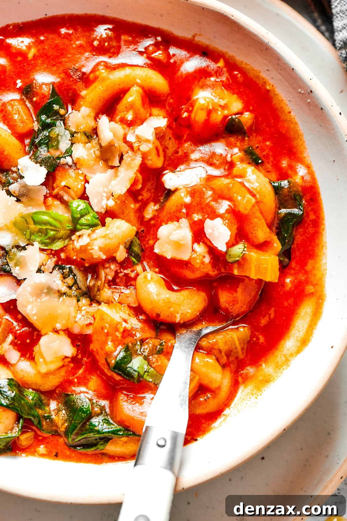 Spoon stirring through tomato soup with spinach and pasta.
