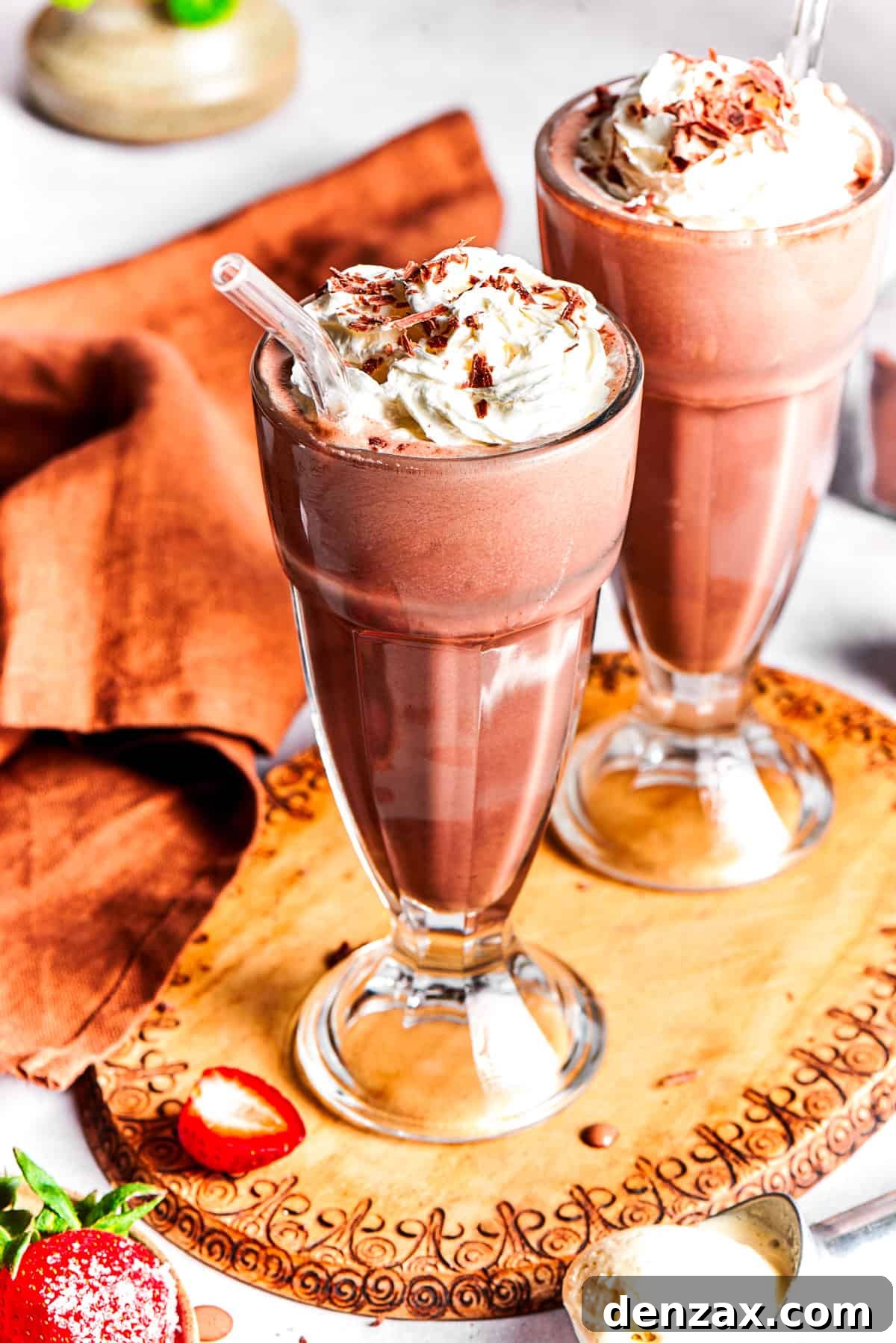 Two glasses of chocolate milkshake set on a wooden tray.
