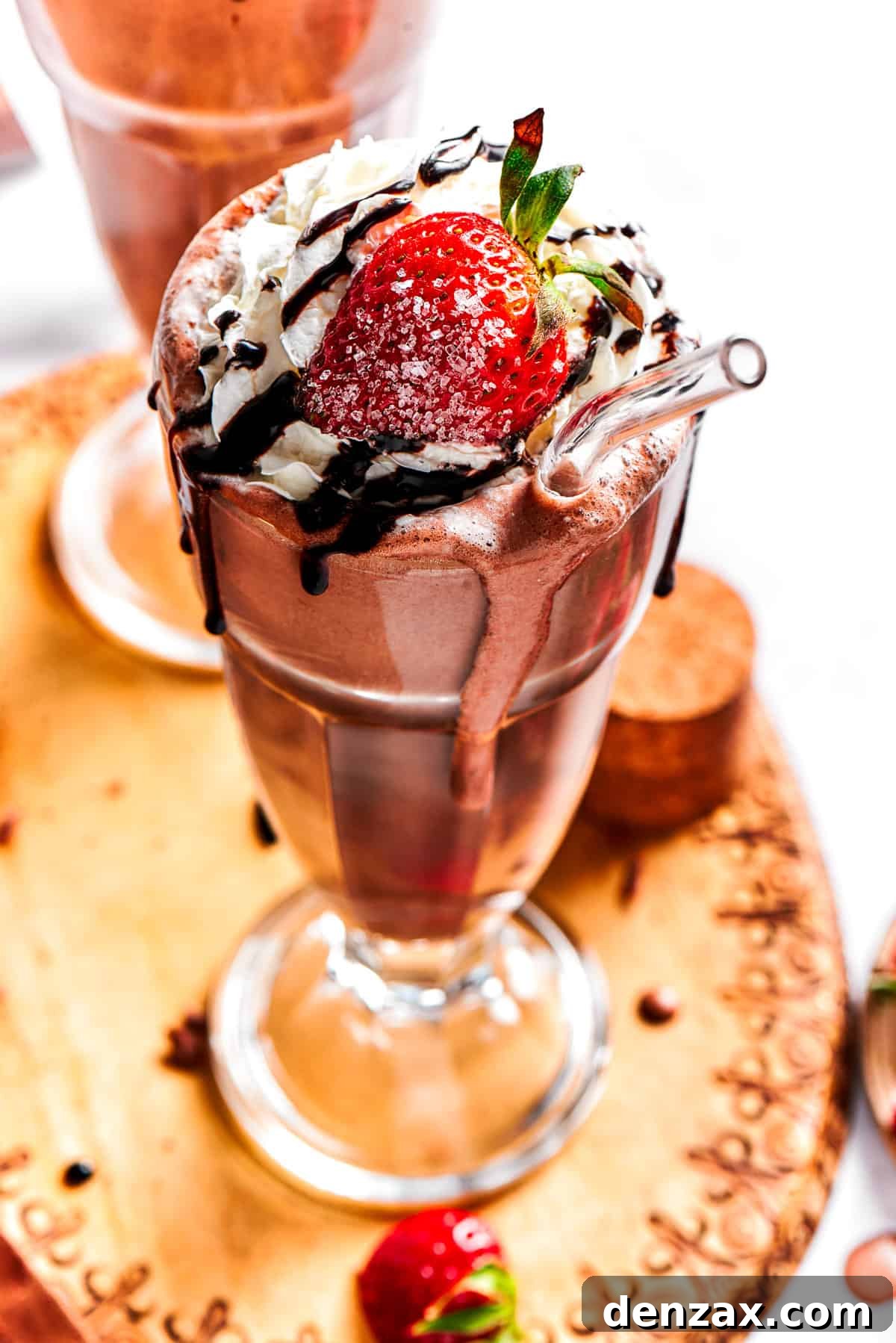 Chocolate milkshake served in a tall glass and garnished with whipped cream, strawberries, and a chocolate drizzle.