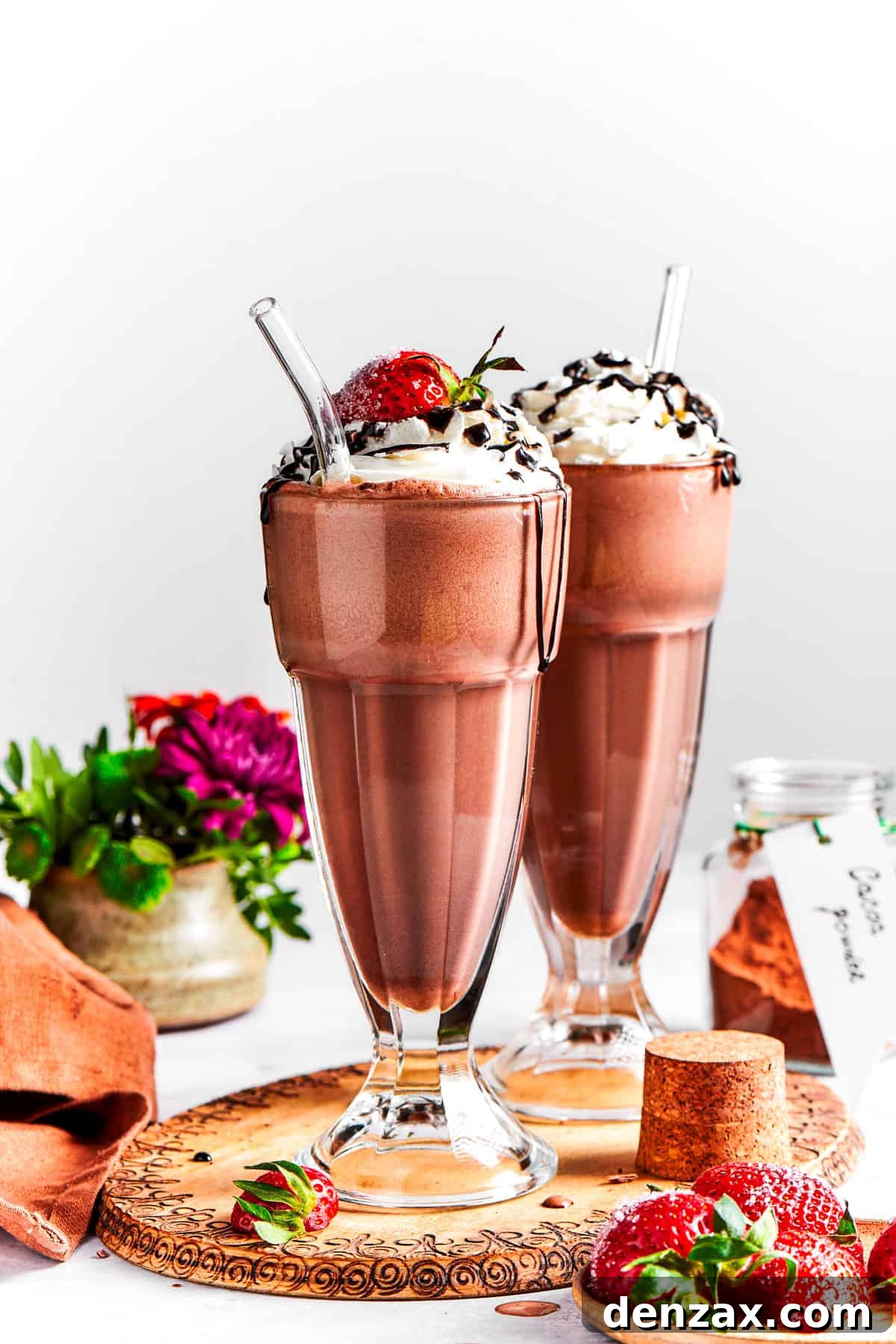 Chocolate milkshake served in tall glasses and garnished with whipped cream, strawberries, and a chocolate drizzle.