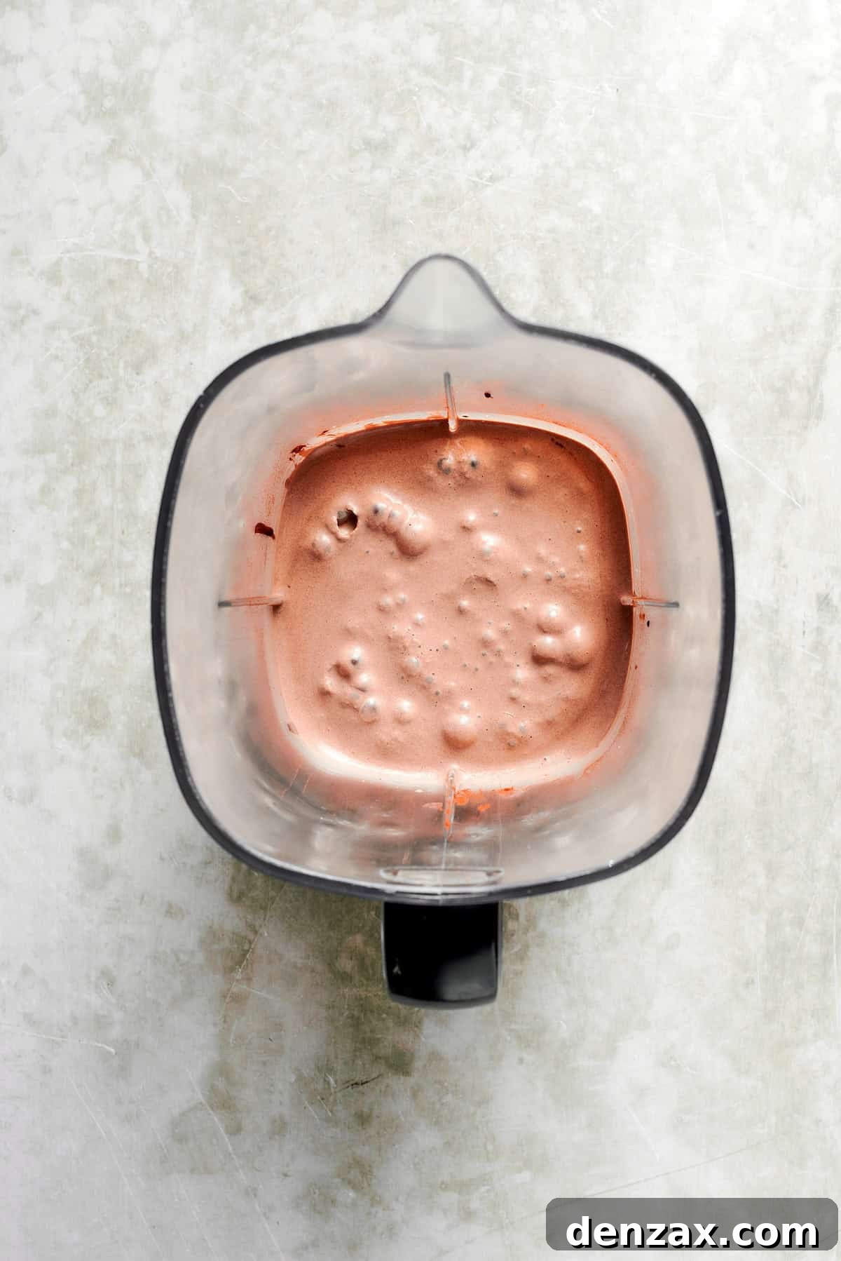 A blender holds a blended chocolate milkshake.
