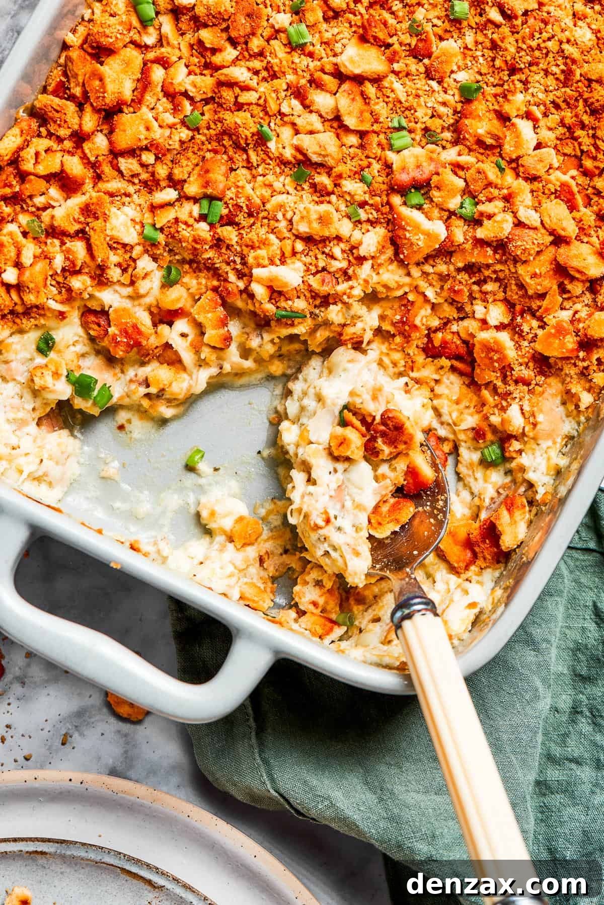 A serving spoon scooping out million dollar chicken casserole from a baking dish.