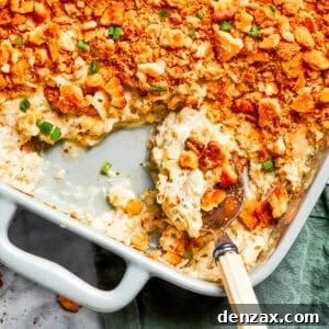 A serving spoon scooping out million dollar chicken casserole from a baking dish.