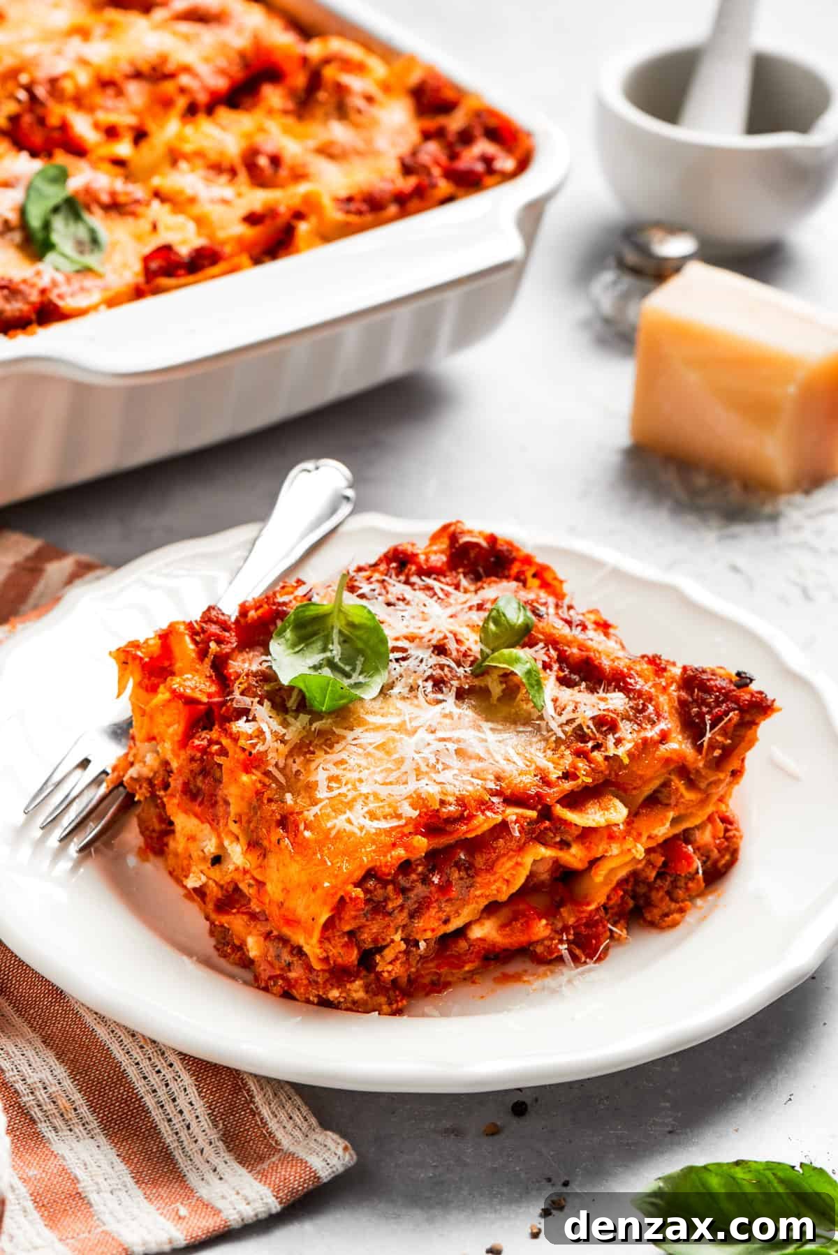 A serving of homemade beef lasagna served on a dinner plate with a fork.