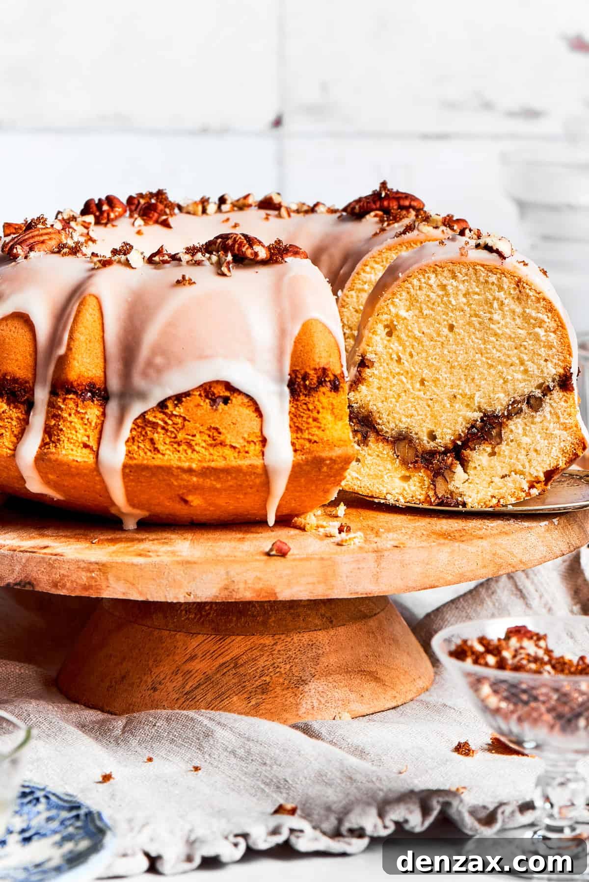 An easy recipe for Sock It To Me Cake, a tender coffee cake with a ribbon of brown sugar, cinnamon and toasted pecans through the center. Sock it to me, cake served on a tall cake plate with a slice cut out exposing the cinnamon sugar ribbon that goes through the cake.