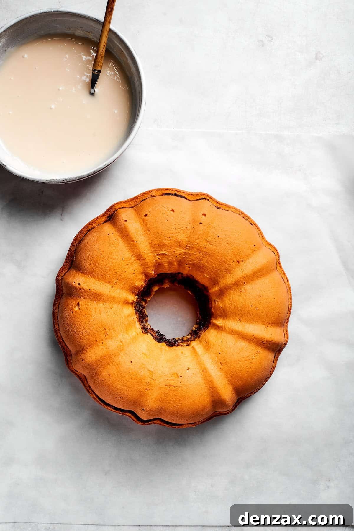 Cooled cake and glaze. A bowl of icing next to a cooled cake.