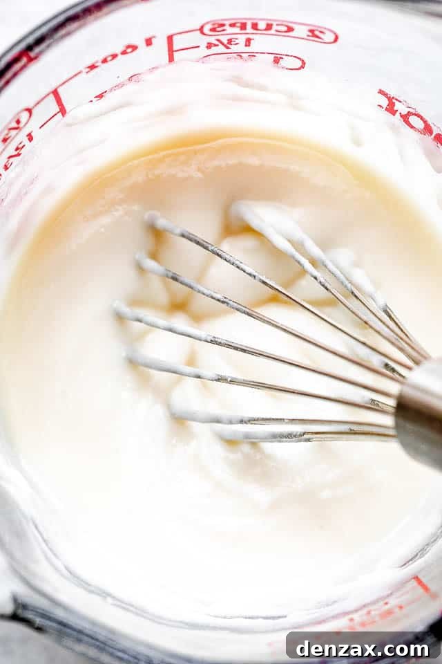 whisking cream cheese frosting in a glass measuring cup