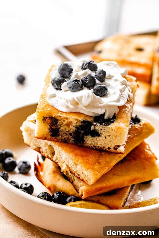 Sheet-Pan Pancakes Recipe: Fluffy Oven-Baked Pancake Tray 2 side shot of stacked sheet pan pancakes topped with whipped cream and blueberries