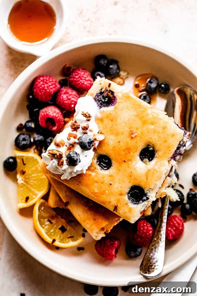 Sheet-Pan Pancakes Recipe: Fluffy Oven-Baked Pancake Tray 5 top shot of squared pancakes topped with whipped cream, berries around the pancakes, and maple syrup to the side