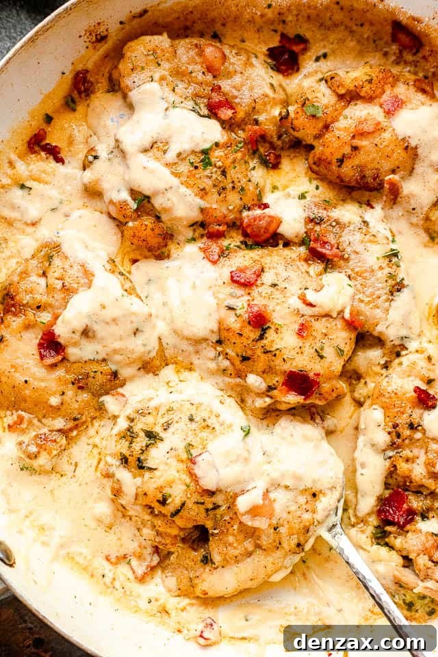 Cream Sauce Chicken Thighs features pan-seared boneless chicken thighs smothered in a decadent cream cheese sauce and topped with bacon! top view of cooked cream sauce chicken thighs in a white skillet with a silver serving spoon picking up the food