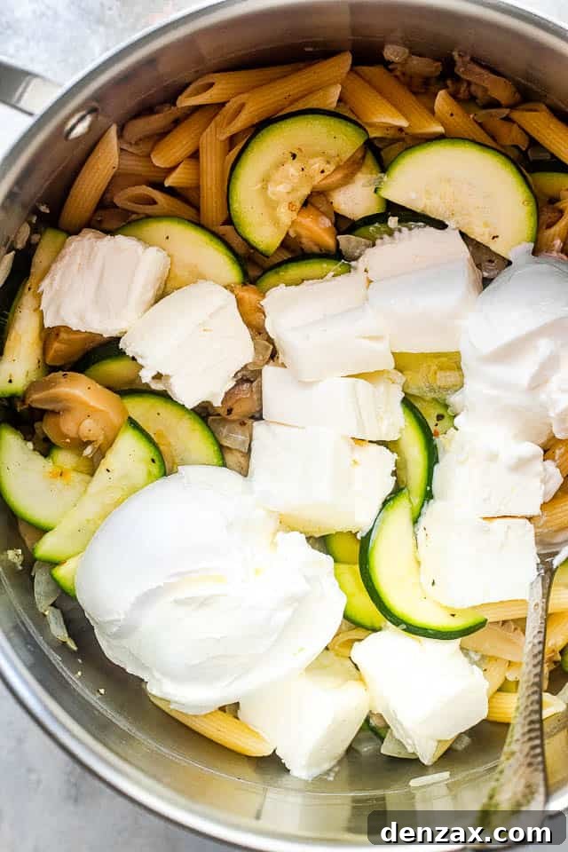 Creamy Baked Pasta with Zucchini and Mushrooms Recipe 4 overhead shot of a silver pot filled with pasta, zucchini slices, and cubed cream cheese