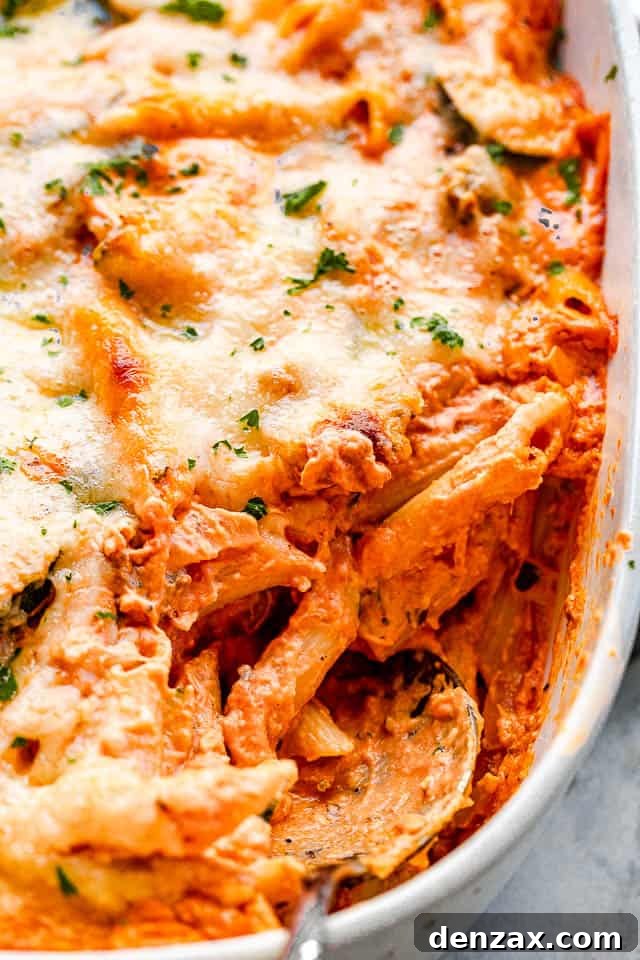 Creamy Baked Pasta with Zucchini and Mushrooms Recipe 5 side view of a cheesy pasta in a baking dish with a serving spoon pulling out the food