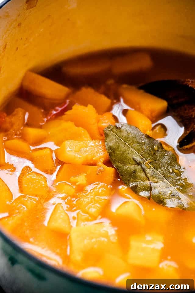 Diced Butternut squash simmering in broth, with a bay leaf set on top of the liquid.