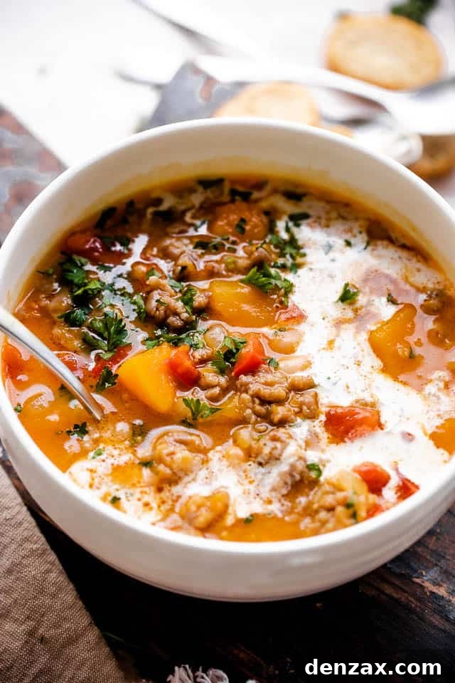 Side shot of butternut squash and sausage soup with cream in a white soup bowl.