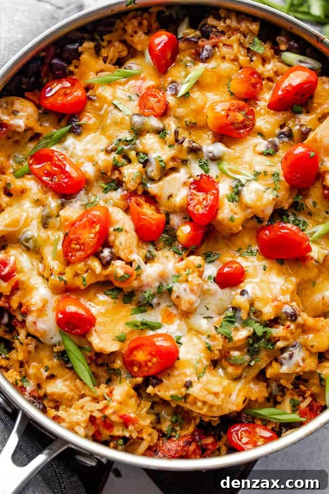 Chicken Burrito Skillet is a festive, one pot meal with juicy chunks of chicken, tender rice, tangy tomatoes, black beans, and cheese. Overhead shot of chicken and rice burrito skillet topped with grape tomatoes.