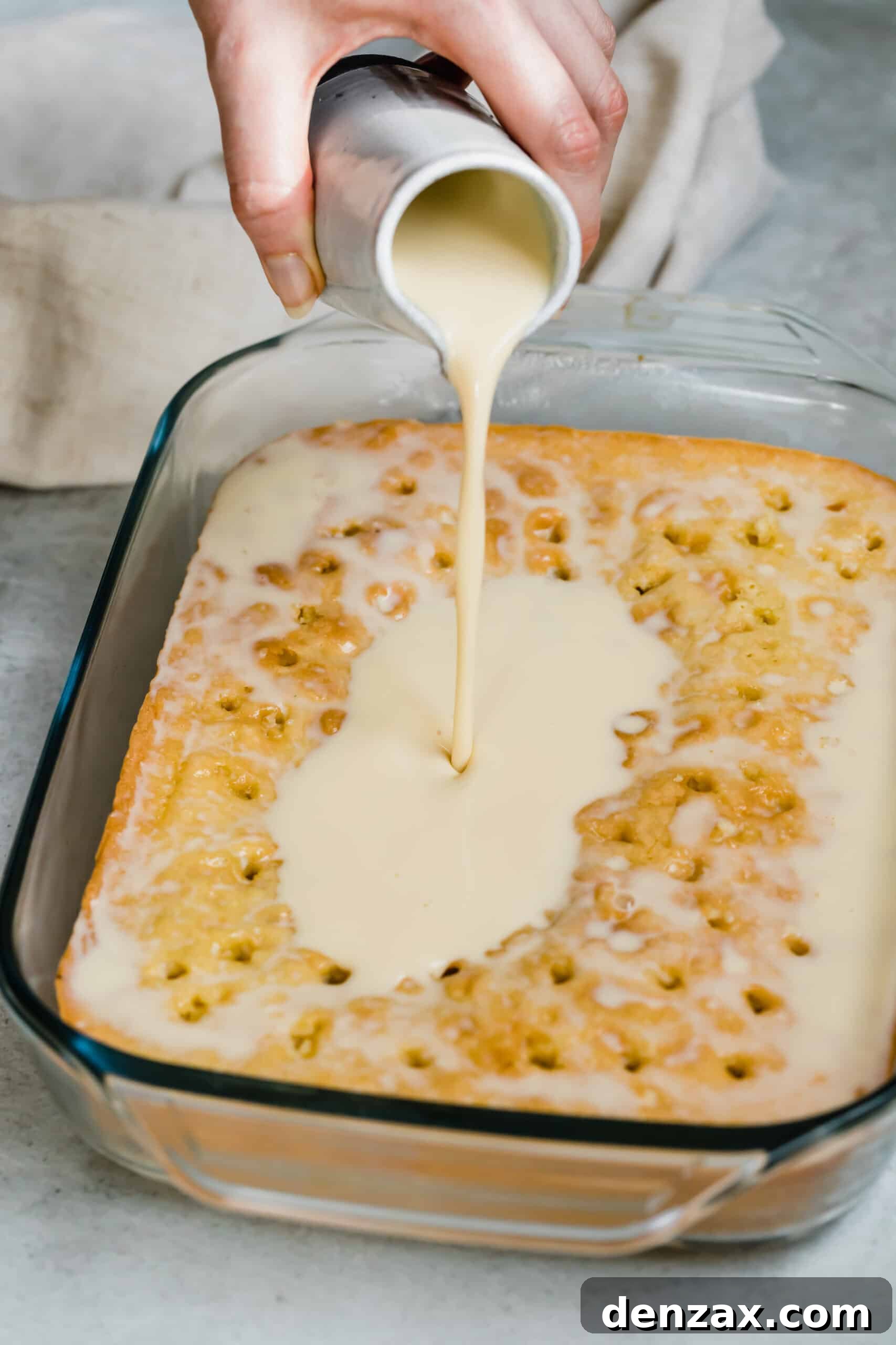Pouring the three milks mixture of a baked sponge cake poked with holes.