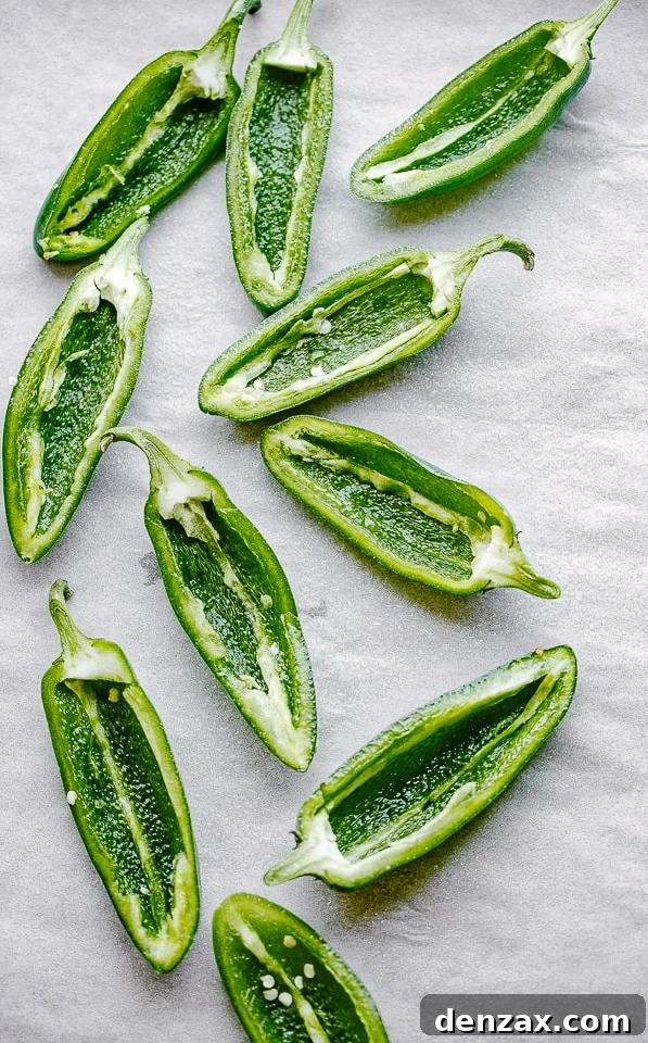 Halved and seeded jalapenos on a parchment-lined surface.