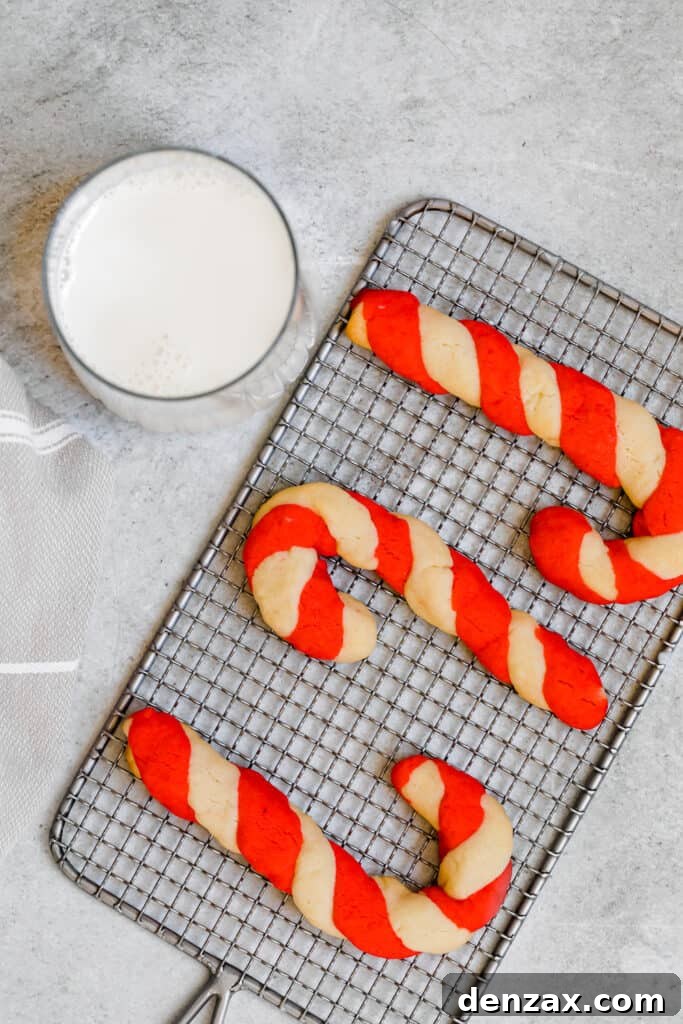 Three Candy Cane Cookies on a Cooling Rack Beside a Glass of Milk