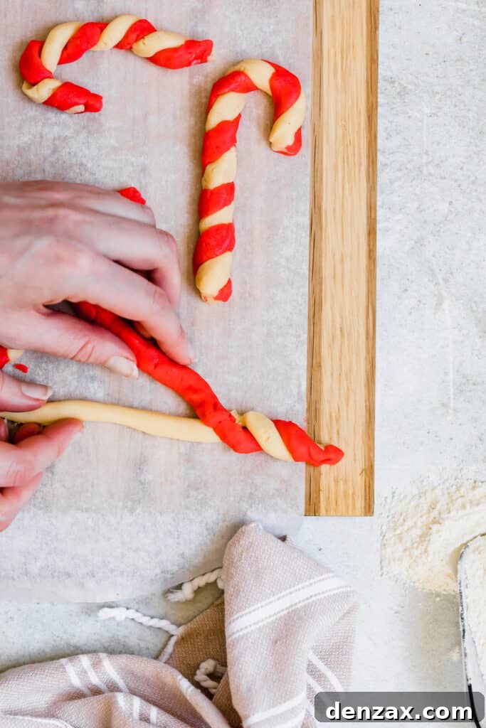 Two Shaped Candy Cane Cookies Next to A Third Being Shaped by Two Hands