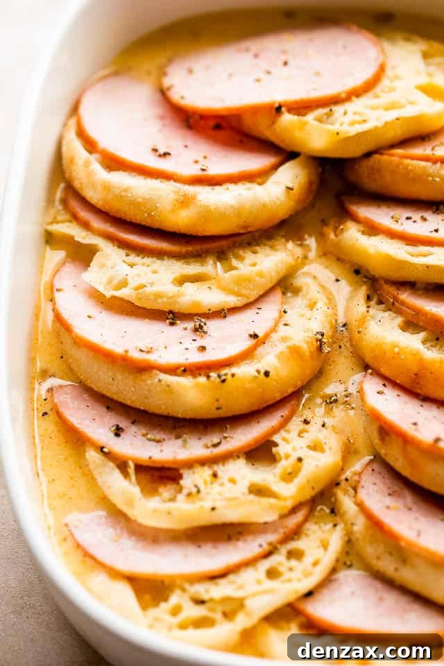 Make-Ahead Eggs Benedict Casserole for Brunch Crowd 5 english muffins and canadian bacon layered in a white baking dish.