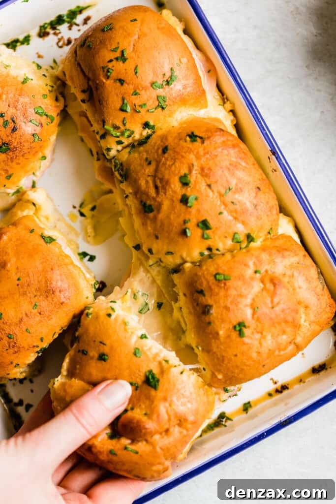 Ham and Swiss Sliders with Honey-Mustard Glaze 3 A Hand Grabbing a Ham and Cheese Slider From a Blue-Rimmed Pan