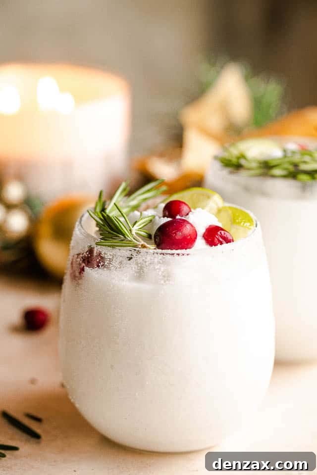 drinking glass filled with margaritas and garnished with lime slices, rosemary sprigs, and cranberries