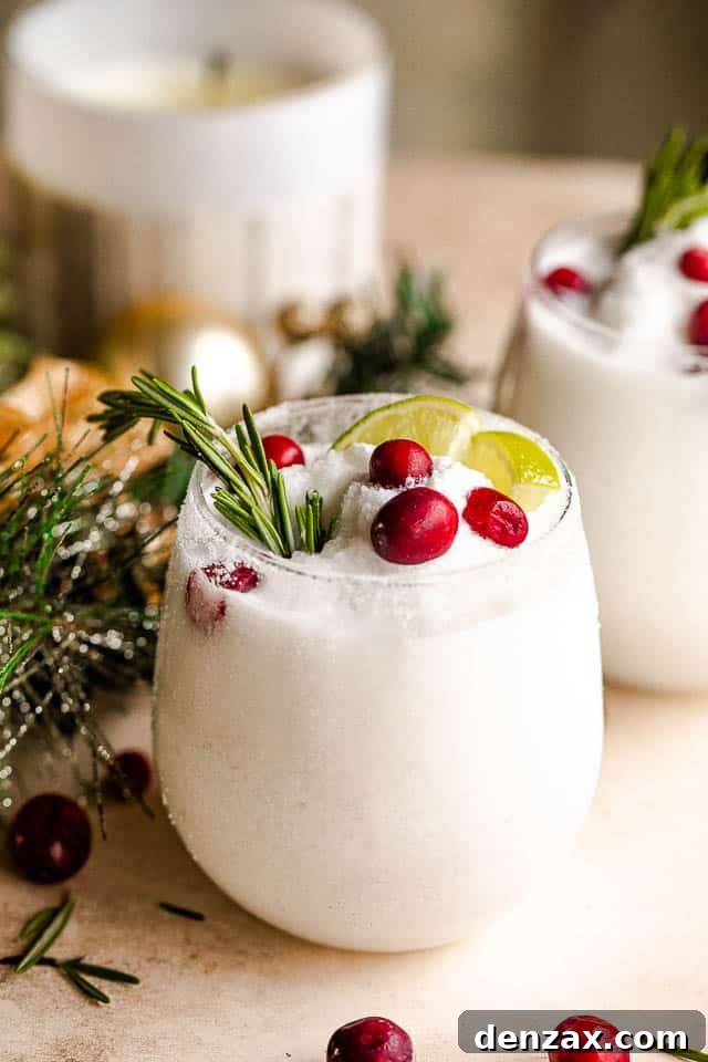 drinking glass filled with margaritas and garnished with lime slices, rosemary sprigs, and cranberries