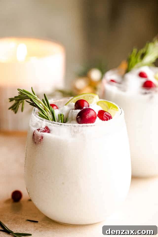 drinking glasses filled with white frozen margaritas and garnished with lime slices, rosemary sprigs, and cranberries