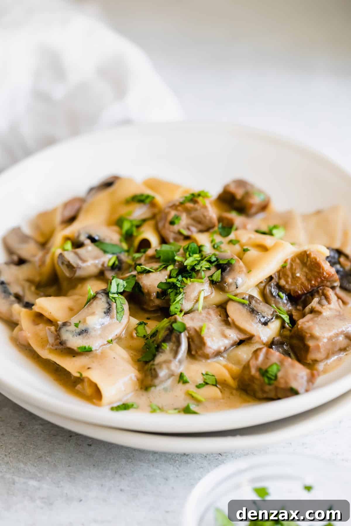 A Plate of Beef Stroganoff Next to a Small Bowl of Chopped Parsley