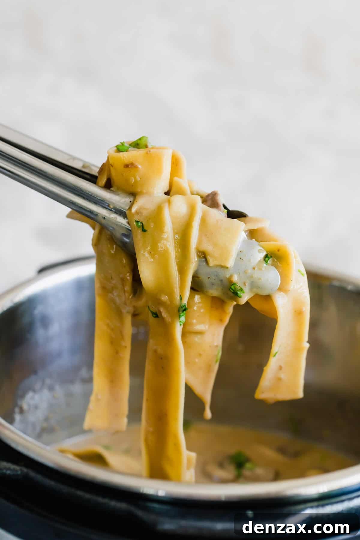 A Pair of Tongs Pulling a Scoop of Beef Stroganoff Out of the Instant Pot