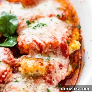 close up side shot of baked pork parmigiana topped with melted cheese and basil leaves.
