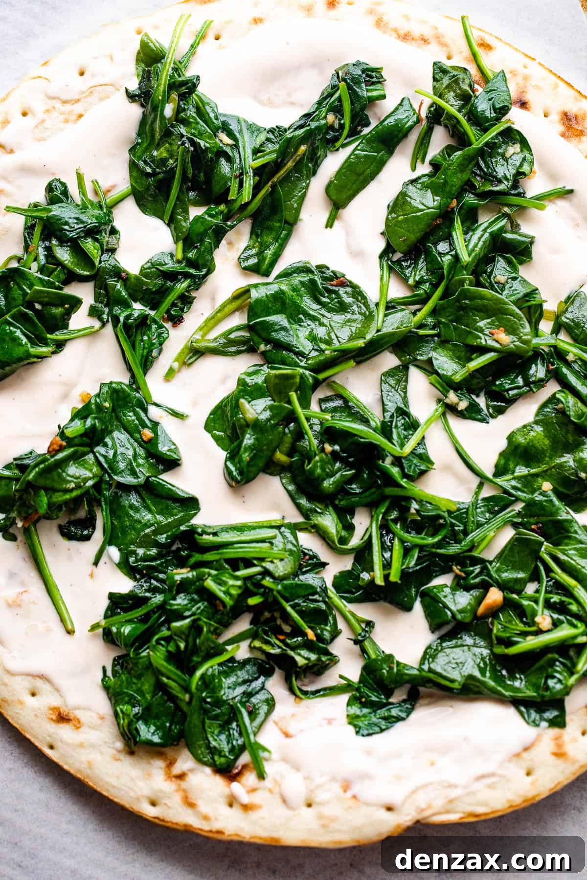 pizza crust topped with alfredo sauce and baby spinach