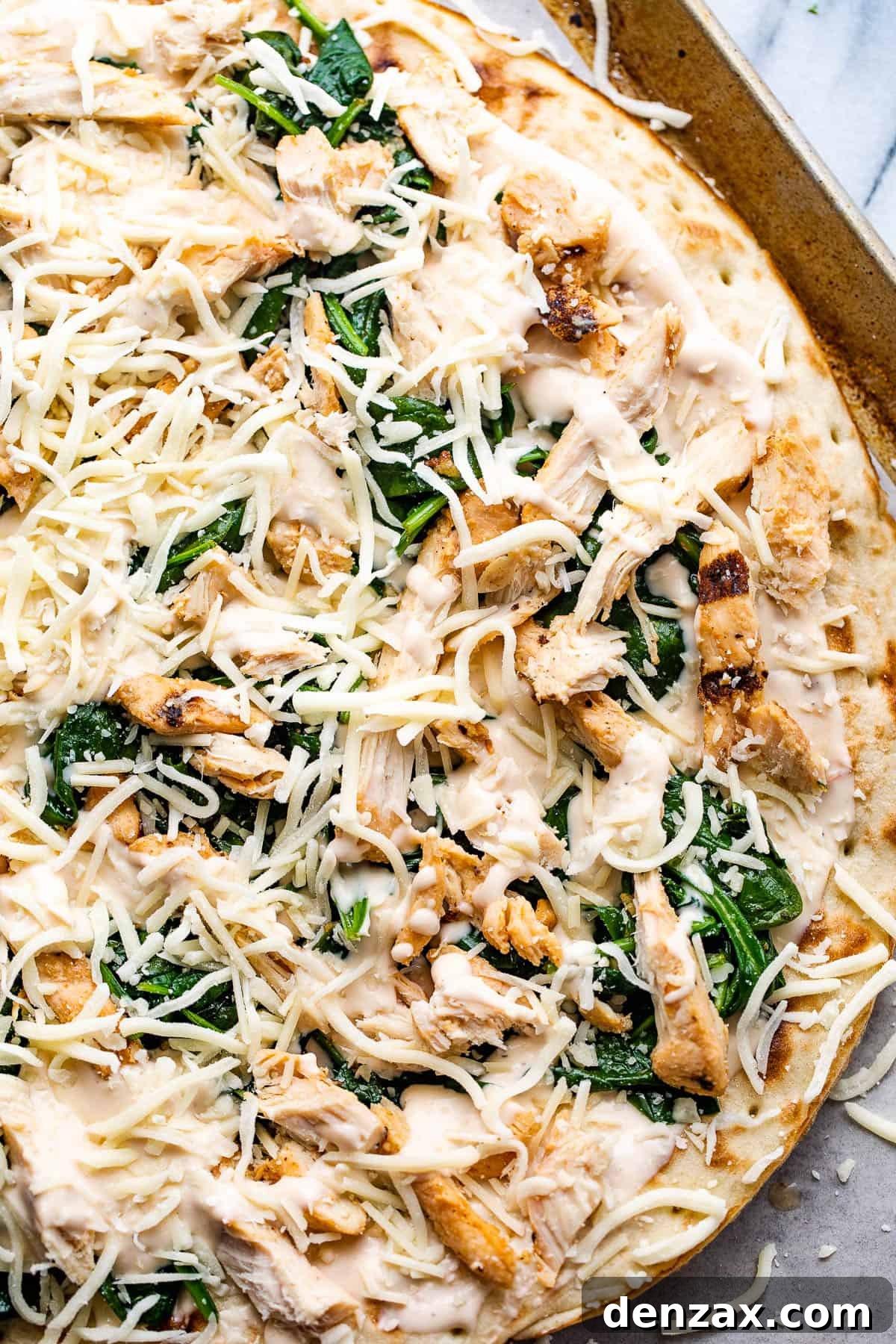 preparing pizza with alfredo sauce, shredded chicken, spinach, and cheese