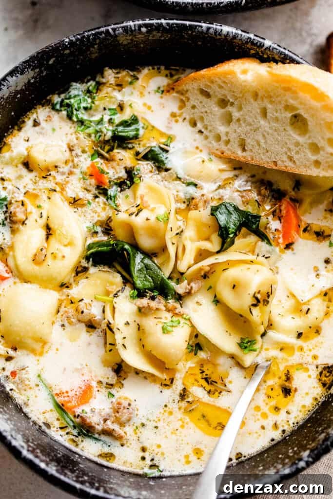close up picture of creamy tortellini soup in a black soup bowl with slice of crusty bread