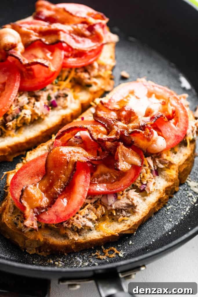 Crispy Tuna Melt Grilled Cheese Sandwich Recipe 6 bread slices topped with flaked tuna, tomatoes, and bacon, all cooking in a black skillet.