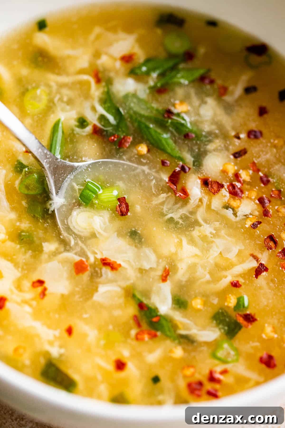 Whip up this simple egg drop soup in just 15 minutes—it might even taste better than the one from your go-to Chinese spot! close up side shot of a bowl with egg drop soup garnished with green onions and red pepper flakes