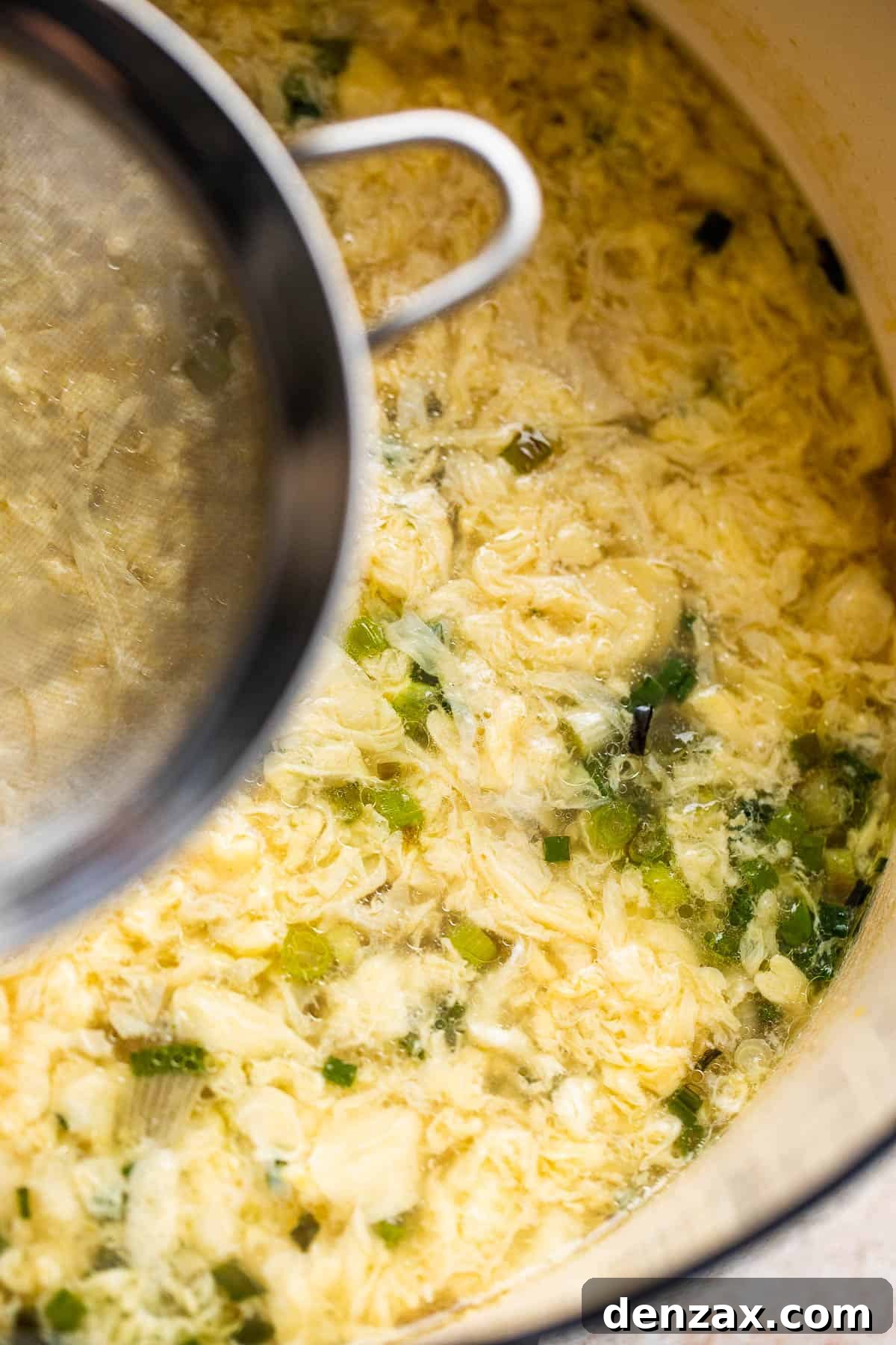 Whip up this simple egg drop soup in just 15 minutes—it might even taste better than the one from your go-to Chinese spot! dropping an egg inside a pot with a mesh sieve