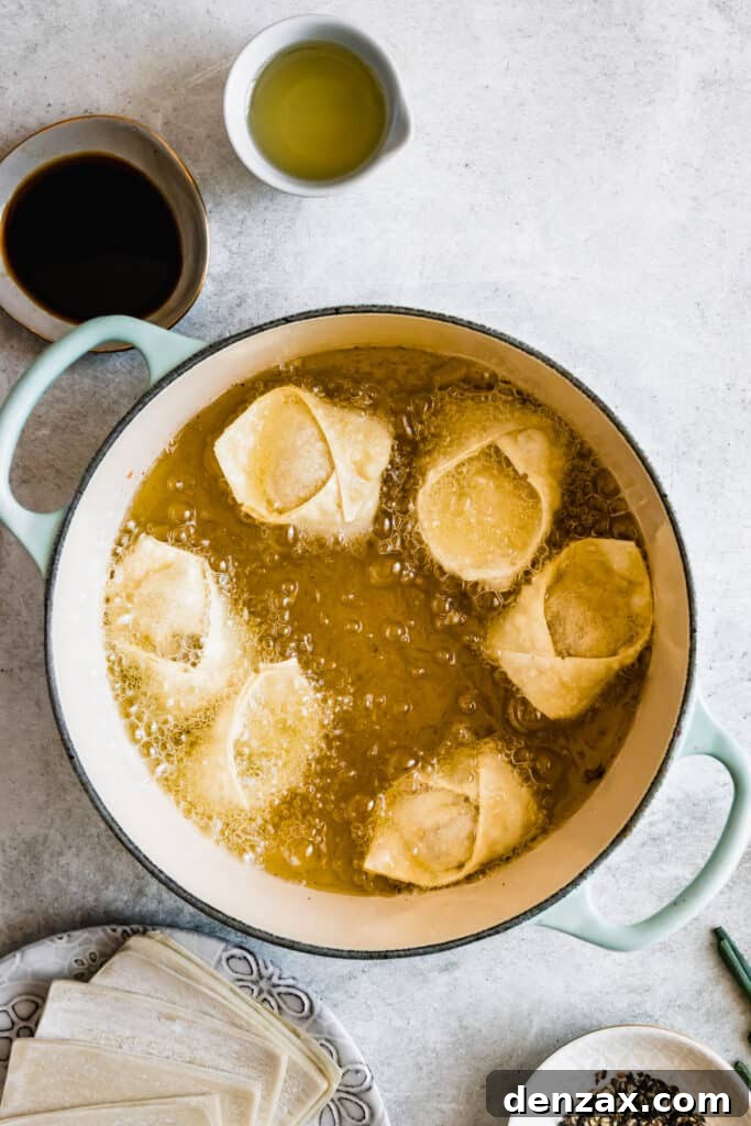 Crispy Crab Rangoon Wontons Recipe: Creamy Crab-Filled Appetizers 8 Crab rangoon wontons being fried in oil