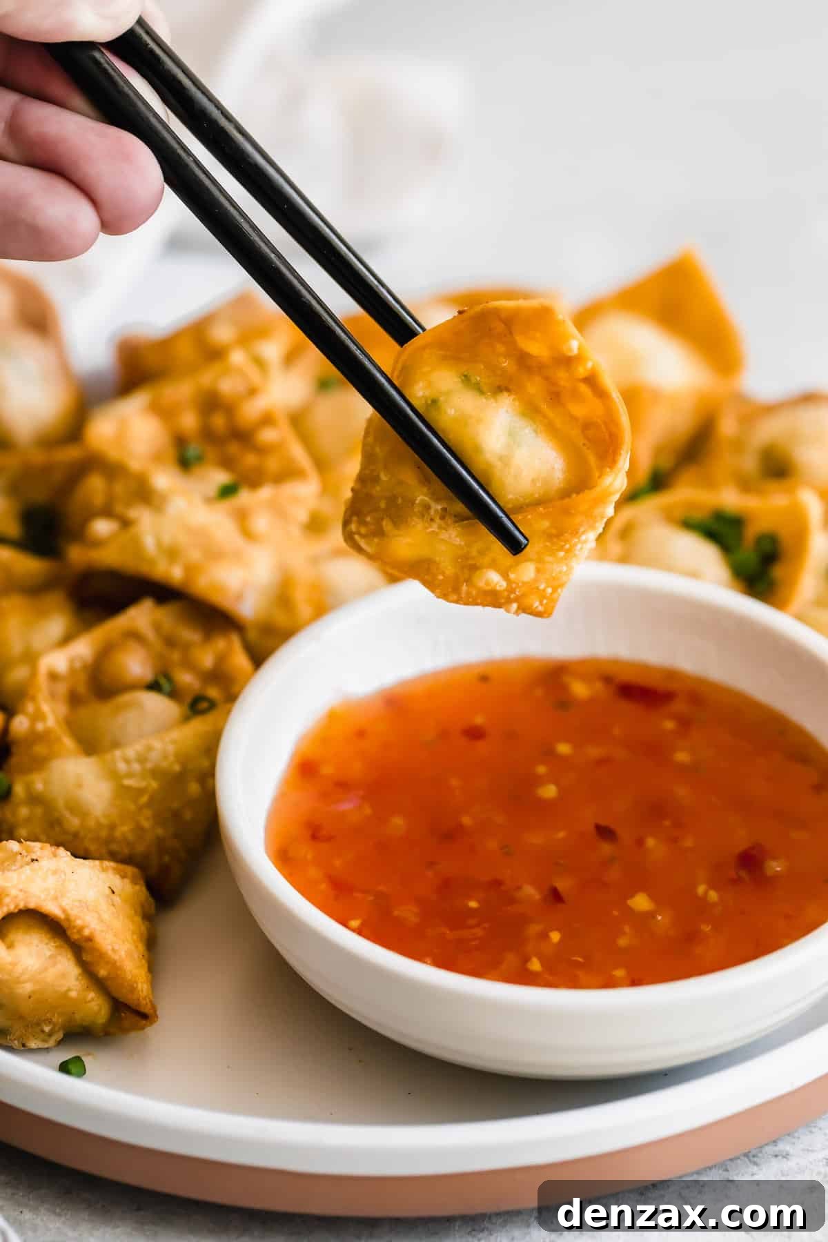 Crispy Crab Rangoon Wontons Recipe: Creamy Crab-Filled Appetizers 10 holding chopsticks and dipping crab rangoon wonton in dipping sauce