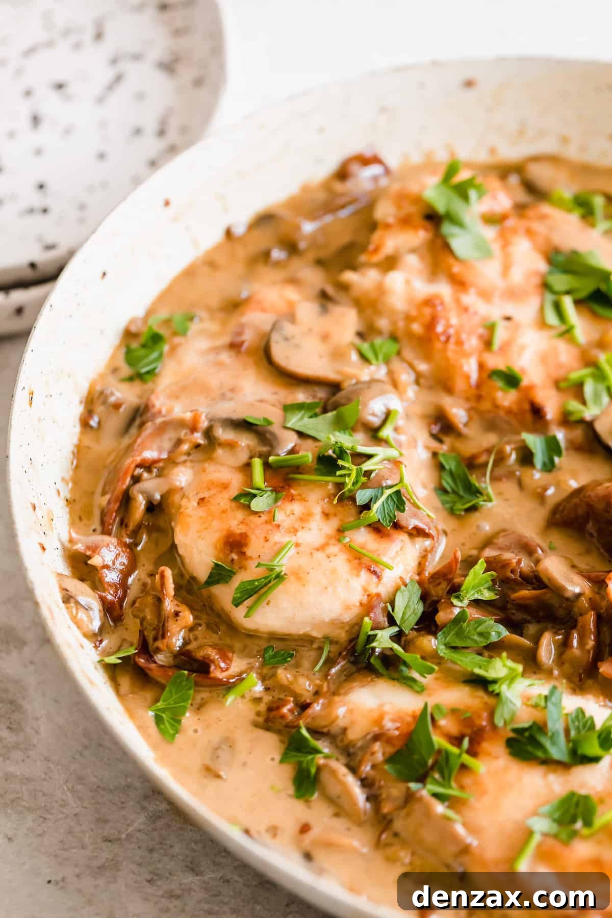 Creamy chicken marsala in a white bowl sprinkled with herbs.