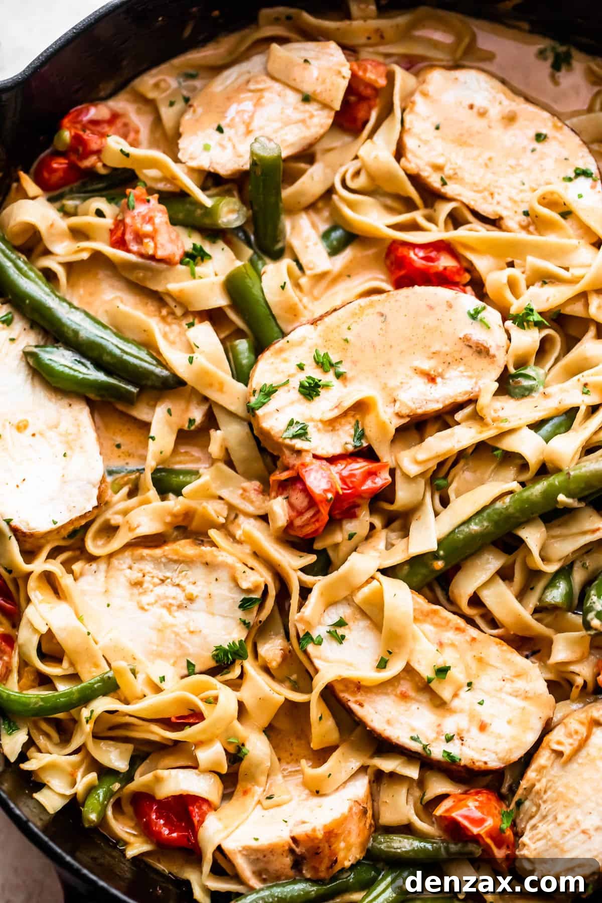 fettuccine pasta in creamy sauce with slices of blackened chicken, tomatoes, and green beans