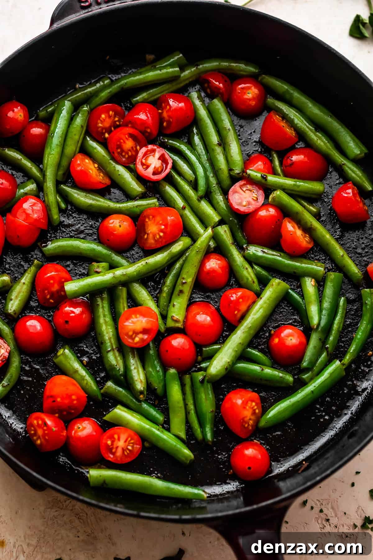 overhead shot of pan frying cherry tomatoes and green beans in a cast iron skillet
