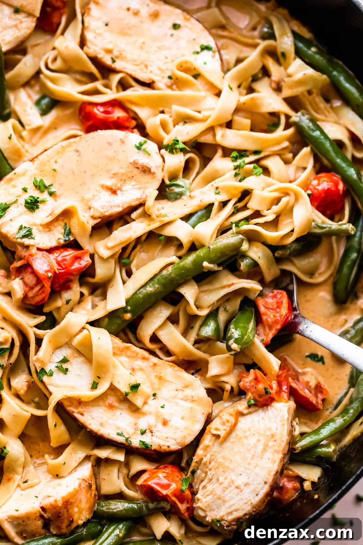fettuccine pasta in creamy sauce with slices of blackened chicken, tomatoes, and green beans