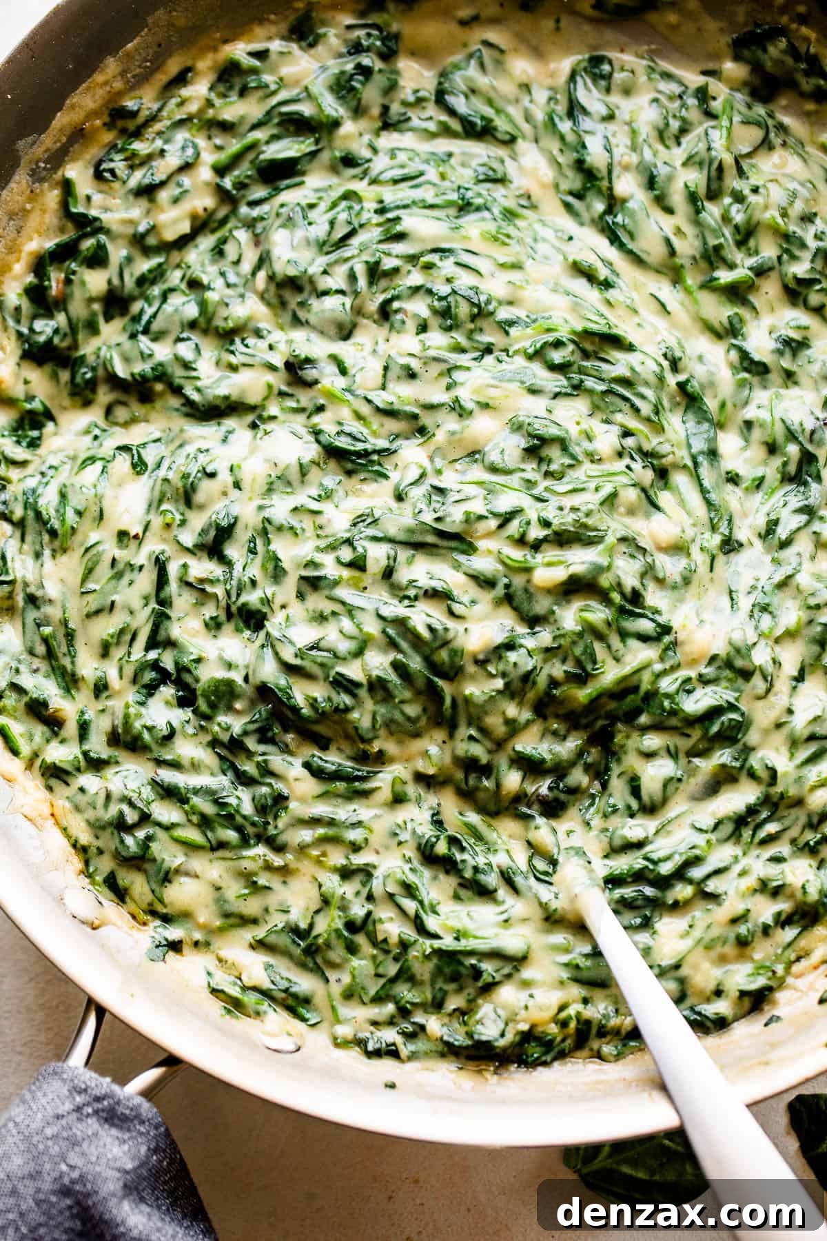 Creamed Spinach is a creamy, gourmet side dish prepared with buttery wilted spinach in a homemade velvety butter sauce. overhead picture of creamed spinach cooking in a large skillet