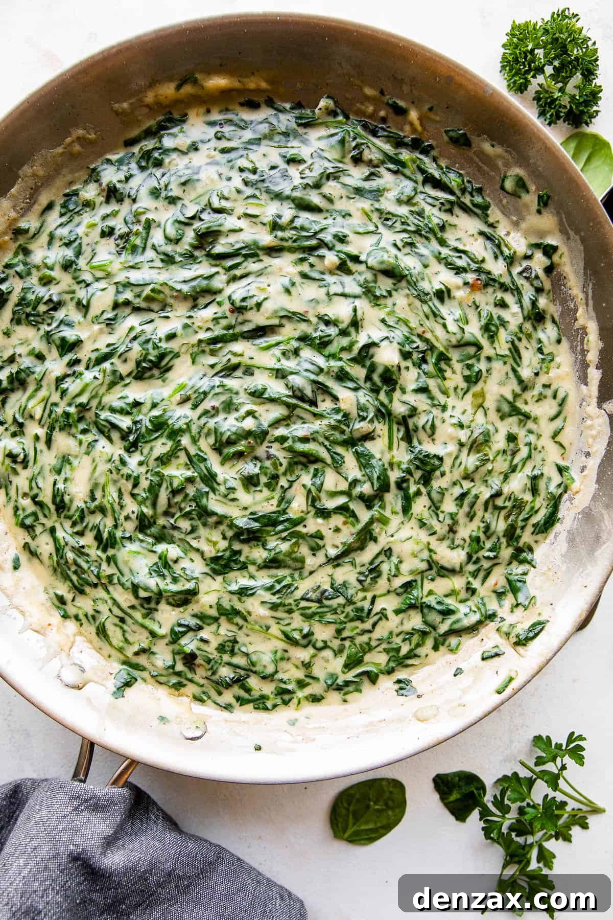 Creamed Spinach is a creamy, gourmet side dish prepared with buttery wilted spinach in a homemade velvety butter sauce. overhead picture of creamed spinach cooking in a large skillet.