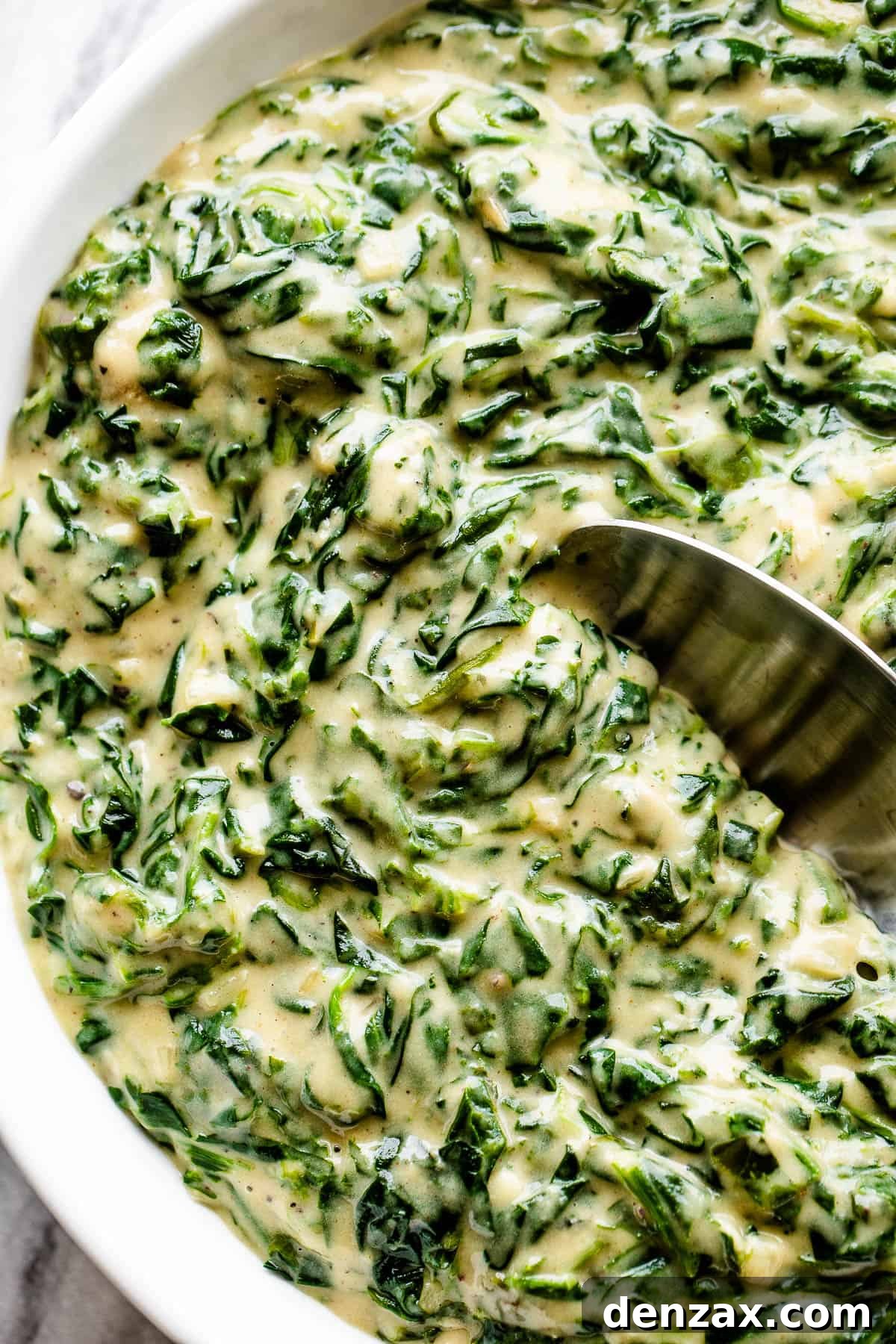 Creamed Spinach is a creamy, gourmet side dish prepared with buttery wilted spinach in a homemade velvety butter sauce. served creamed spinach in a white bowl with spoon inside